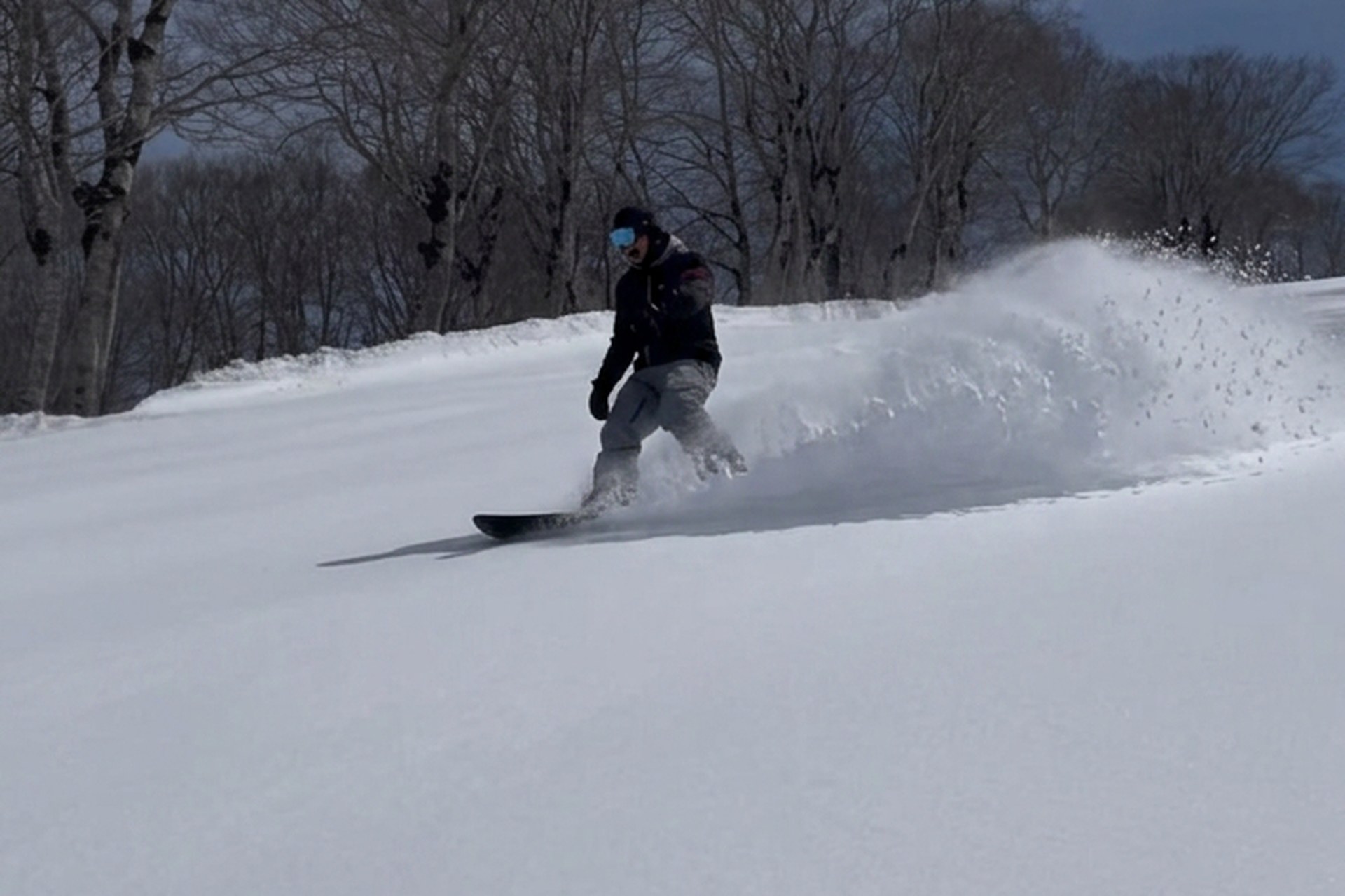 Snowboarder carving through deep powder in Myoko